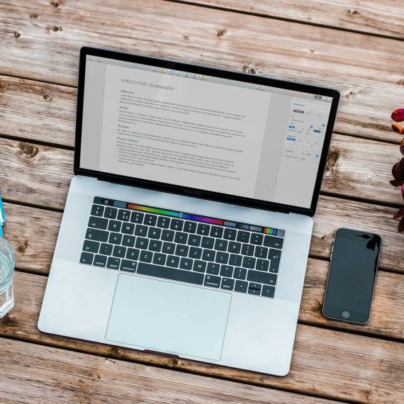 silver MacBook beside space gray iPhone 6 and clear drinking glass on brown wooden top