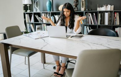 Woman sitting in an office with a laptop, working remotely with a confused expression.